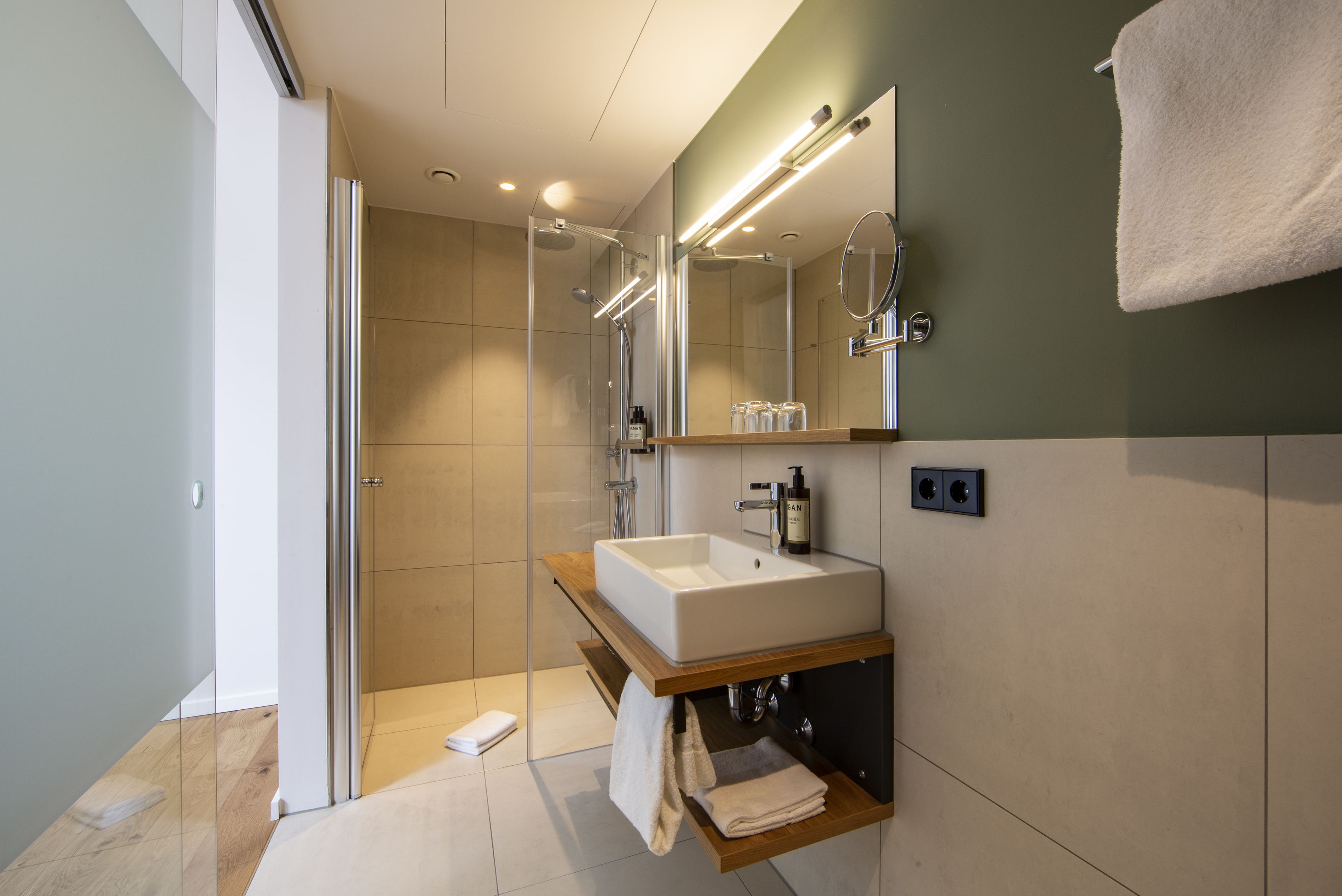 Un baño moderno con ducha de vidrio, lavamanos blanco e iluminación integrada en el espejo.