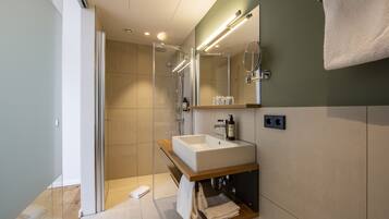 Un baño moderno con ducha de vidrio, lavamanos blanco e iluminación integrada en el espejo.