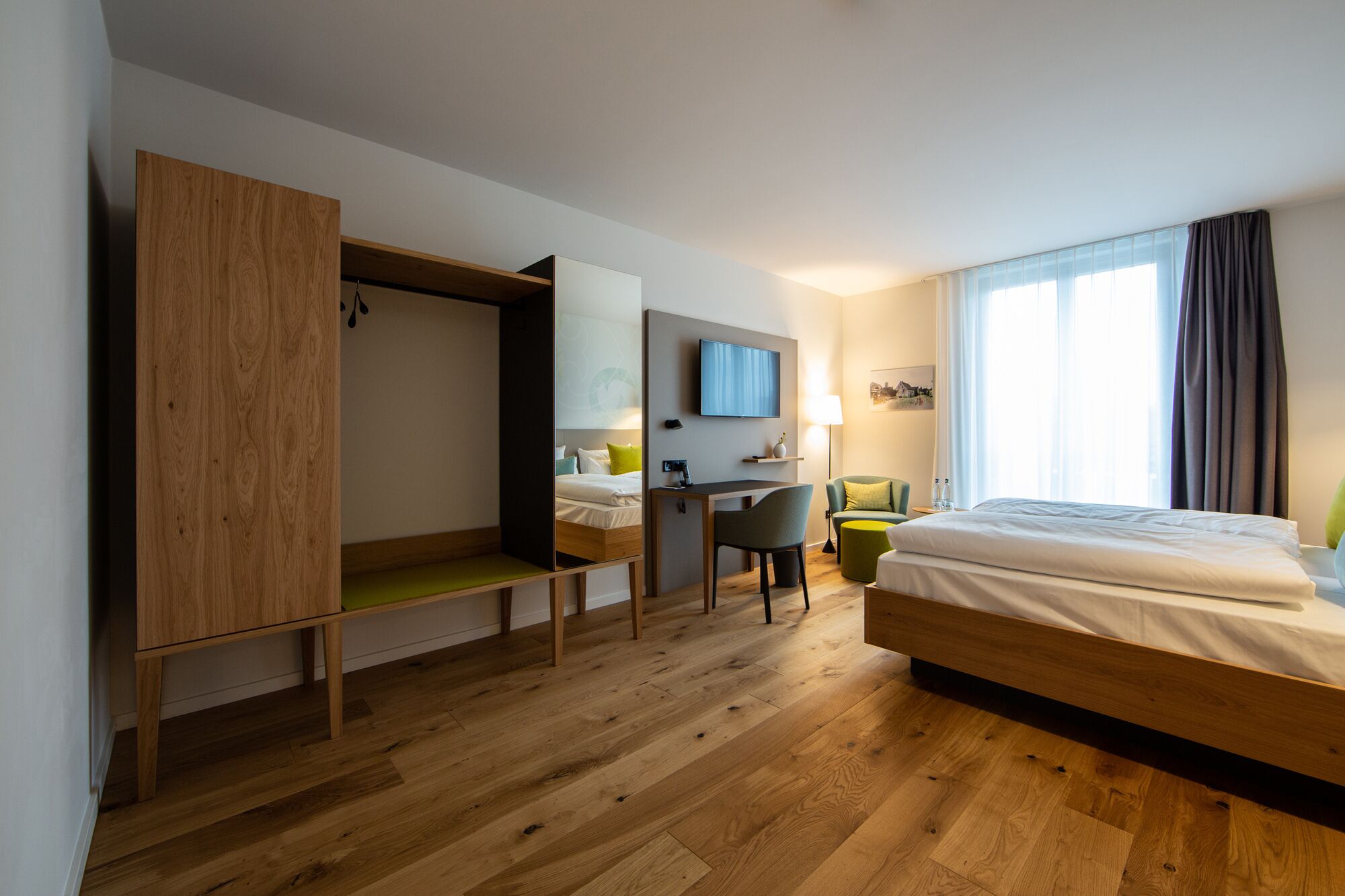 A hotel room with a bed, a desk, a chair, a wardrobe, and a television.