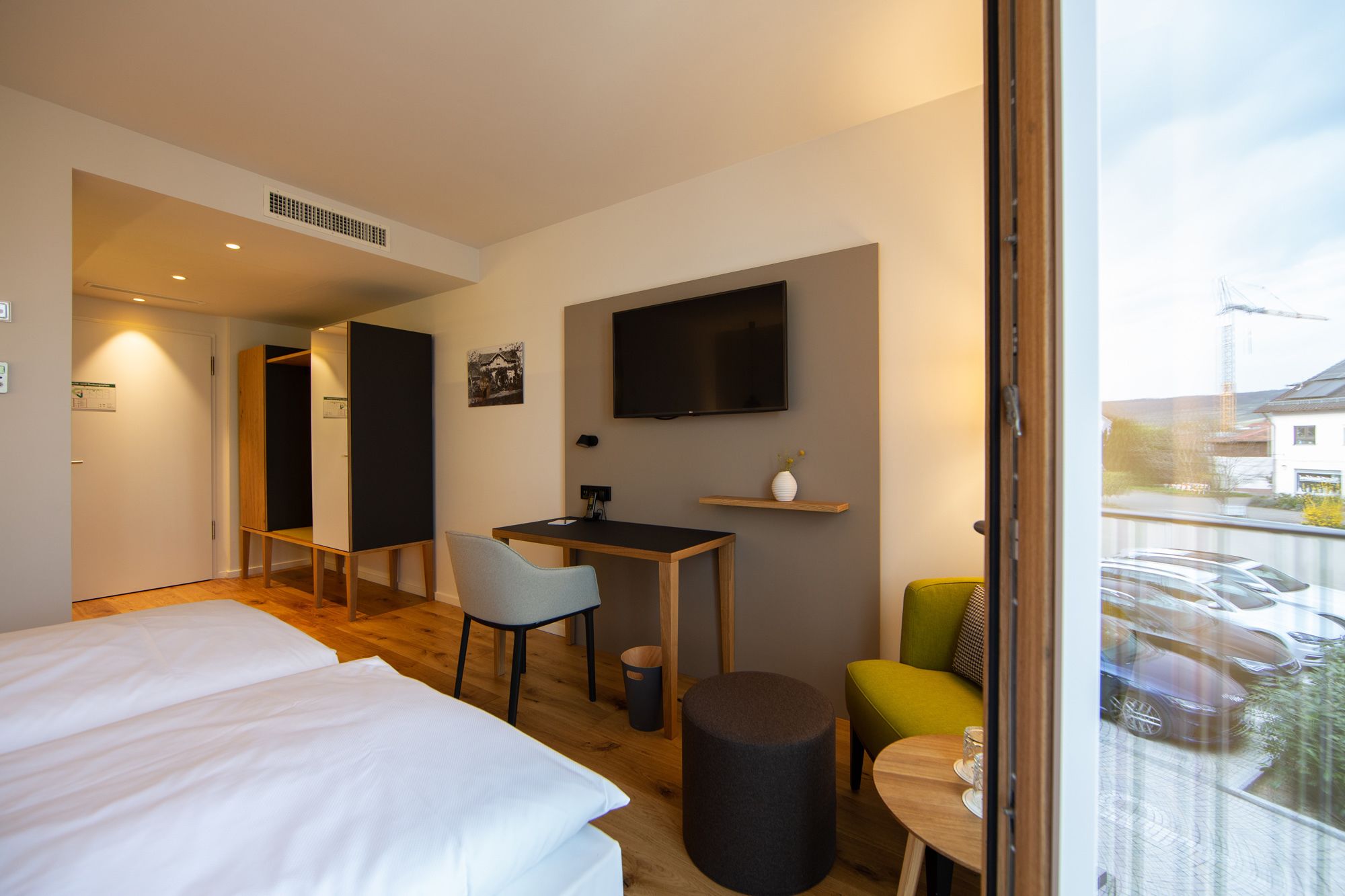 A modern hotel room with a bed, a desk, a chair, a TV, and a balcony with a view of the city.