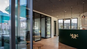 Un intérieur moderne avec un plancher en bois, des cloisons en verre et un comptoir d’accueil vert foncé orné d’un blason.