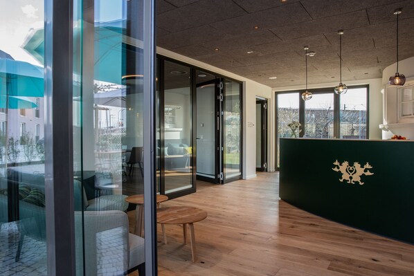 A modern interior with a wooden floor, glass partitions, and a dark green reception desk with a crest. - Gasthaus und Hotel zum Löwen (Eimeldingen)