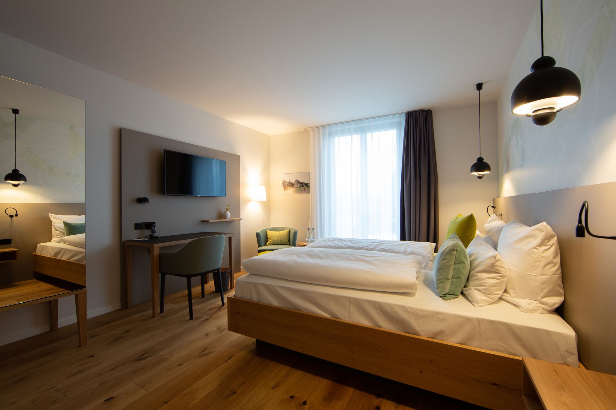 Ein modernes Hotelzimmer mit einem hölzernen Bett, einem Schreibtisch, einem Stuhl, einem Flachbildfernseher und einem großen Fenster mit Vorhängen.