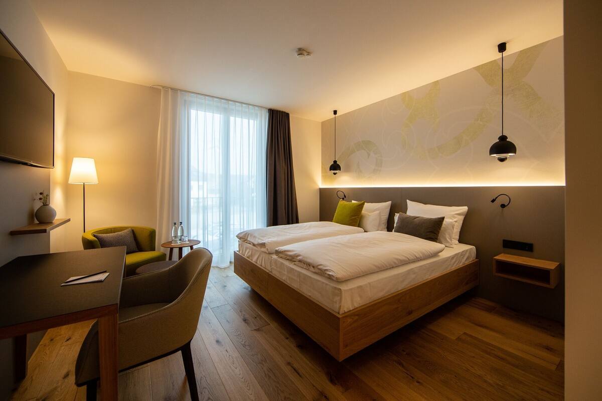Ein modernes Hotelzimmer mit einem großen Bett, einem Schreibtisch, einem Stuhl und Blick ins Freie.