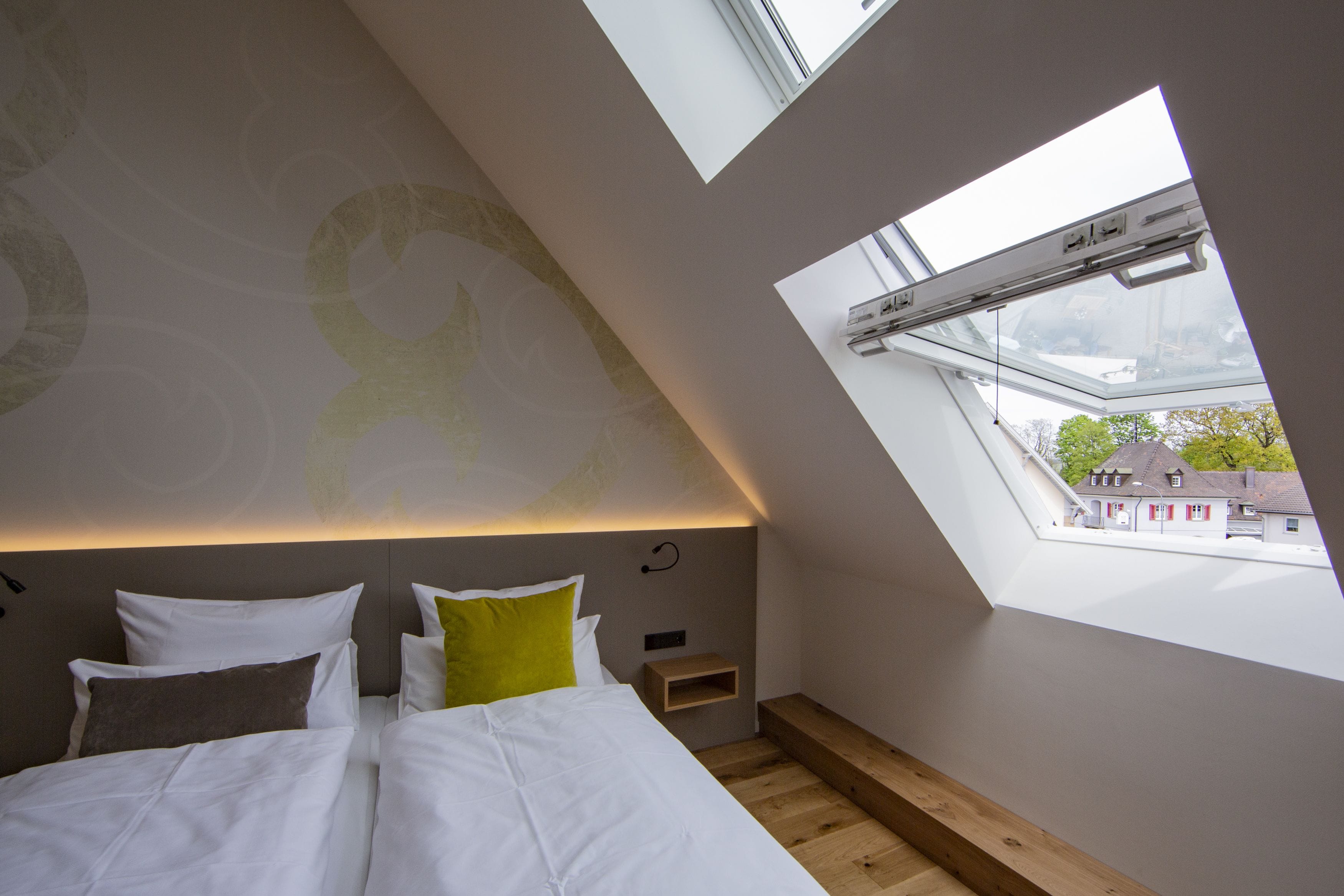 A bedroom with a sloped ceiling, a skylight, and a view of buildings outside.