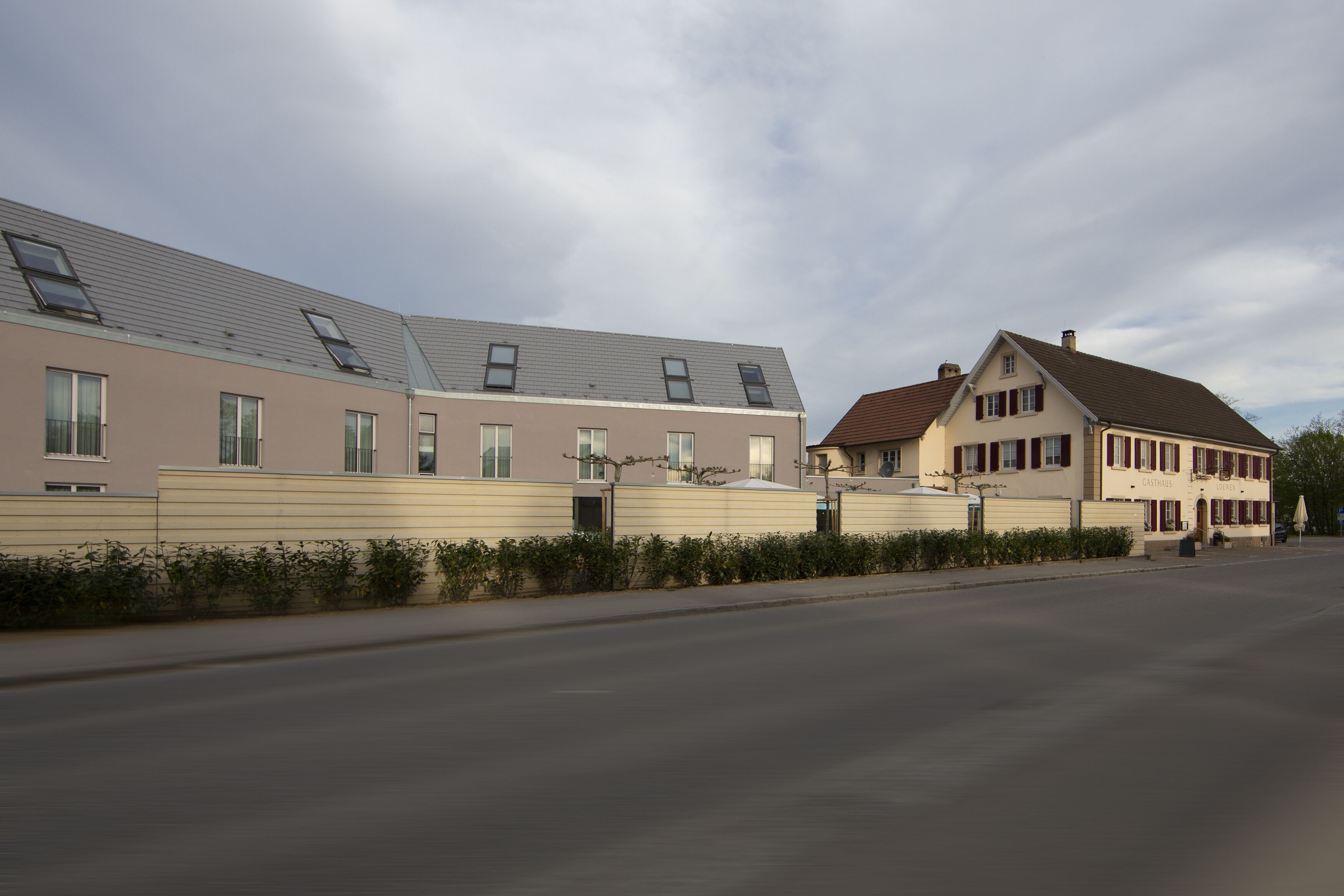 A row of modern residential buildings with flat roofs and large windows, a paved street, and a clear sky.