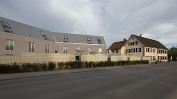 A row of modern residential buildings with flat roofs and large windows, a paved street, and a clear sky.