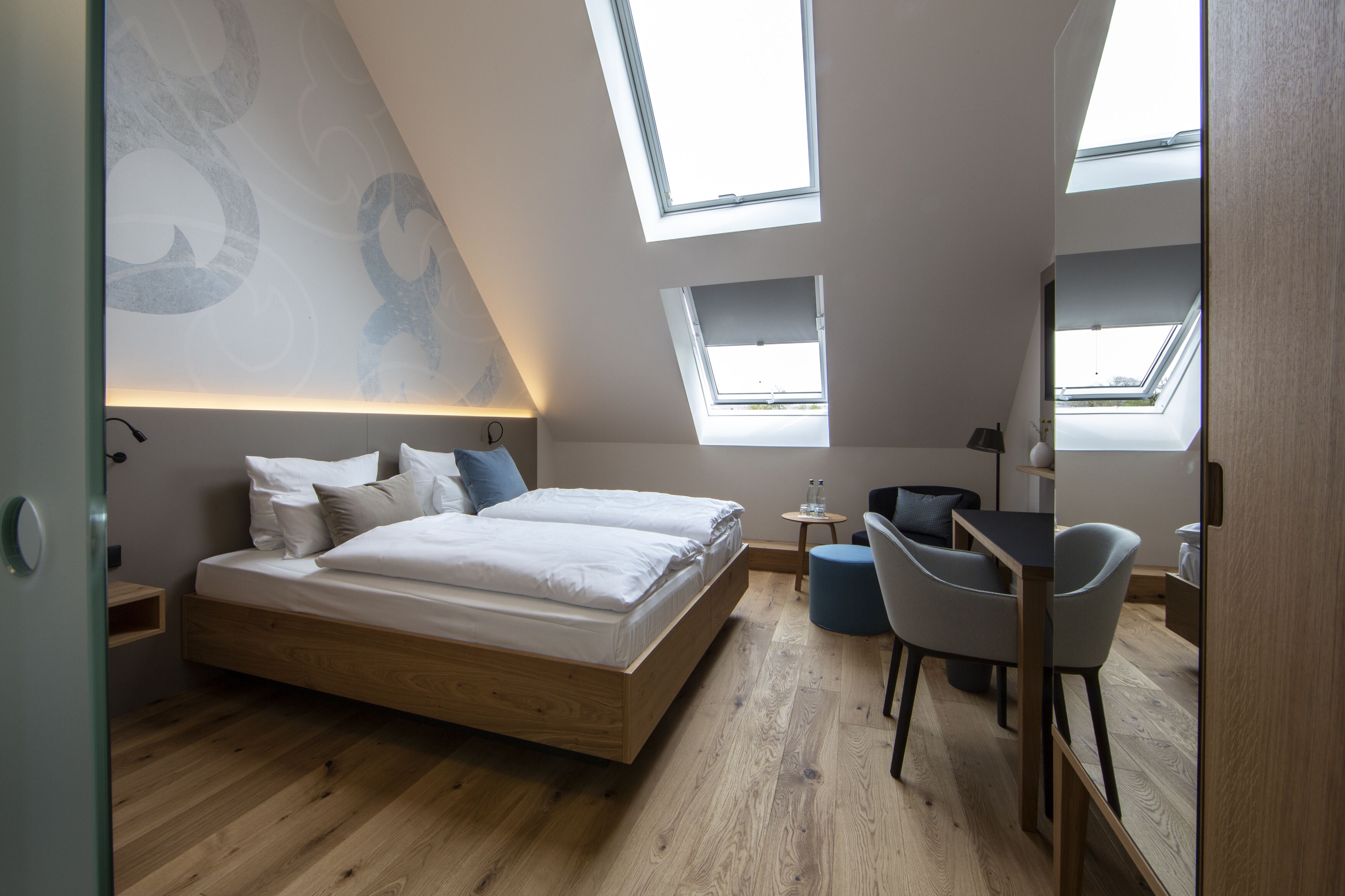 Une chambre moderne avec un lit en mezzanine, des fenêtres de toit, une petite table et deux chaises.