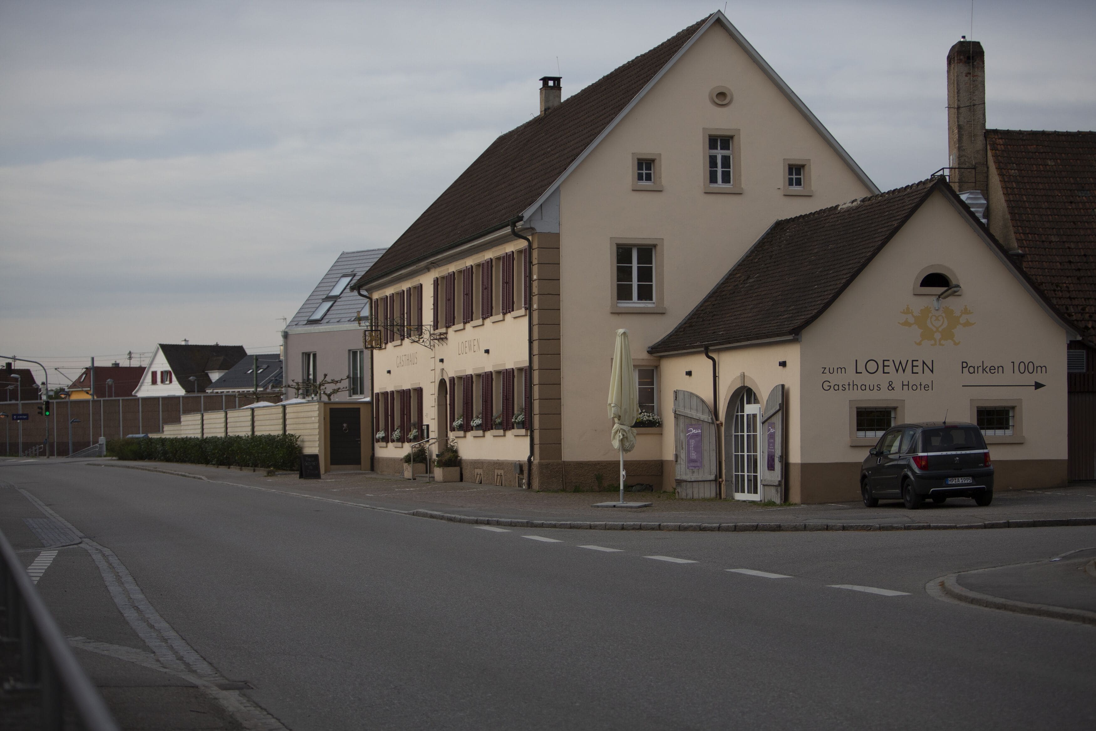 A building with a sign reading "LOEWEN Gasthaus & Hotel" and a car parked in front.