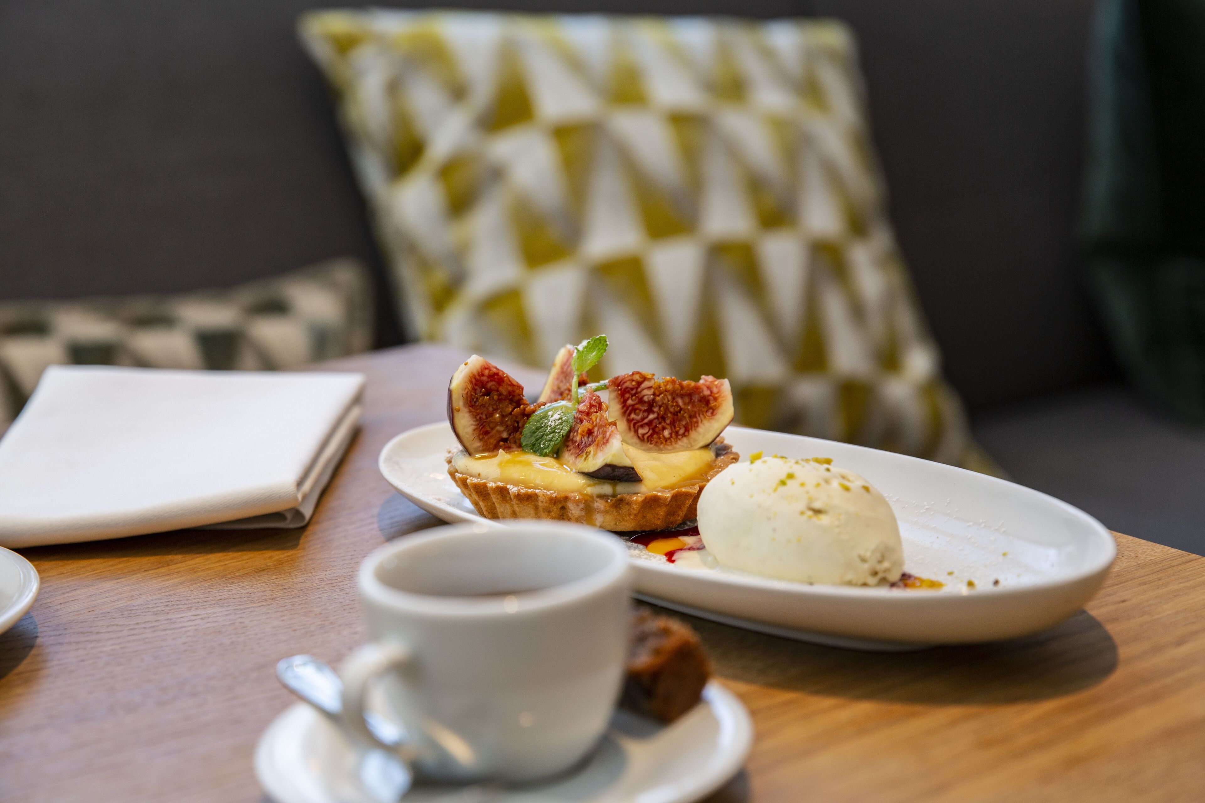 Uma mesa com um prato de sobremesa contendo uma torta, uma bola de sorvete e uma xícara de café.