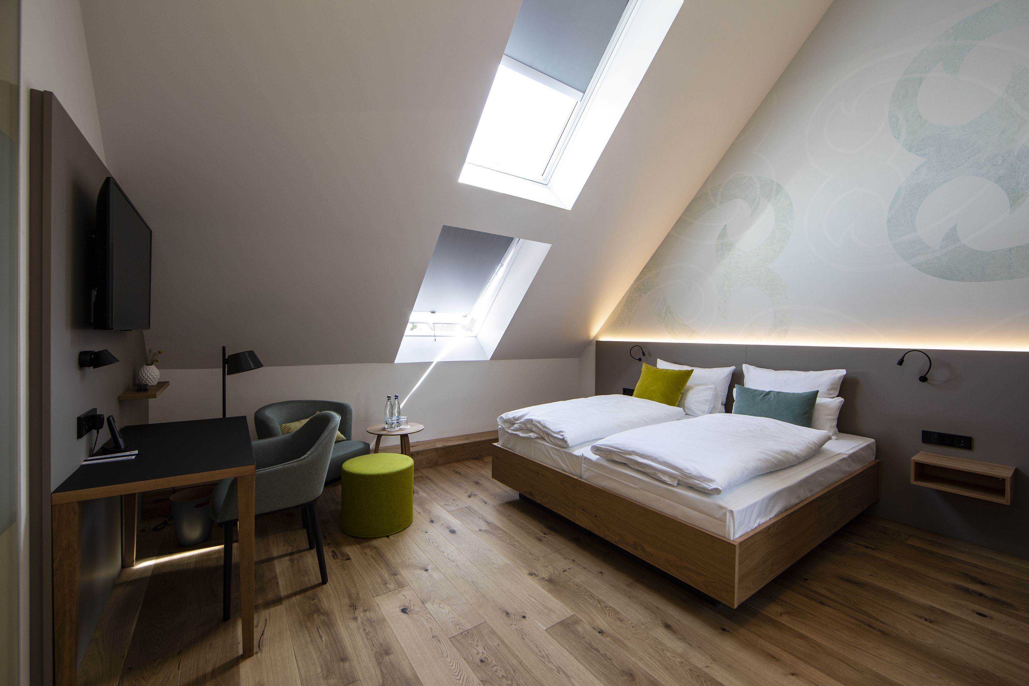 A modern bedroom with a skylight, a desk, a chair, and a bed with pillows.