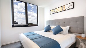 A modern hotel room with a large bed, a view of the sky through a window, and a small round table. - Artel Apartment Hotel Melbourne (Brunswick)
