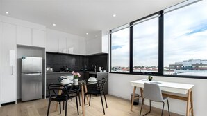 A modern kitchen with a dining area, large windows, and a view of the city. - Artel Apartment Hotel Melbourne (Brunswick)