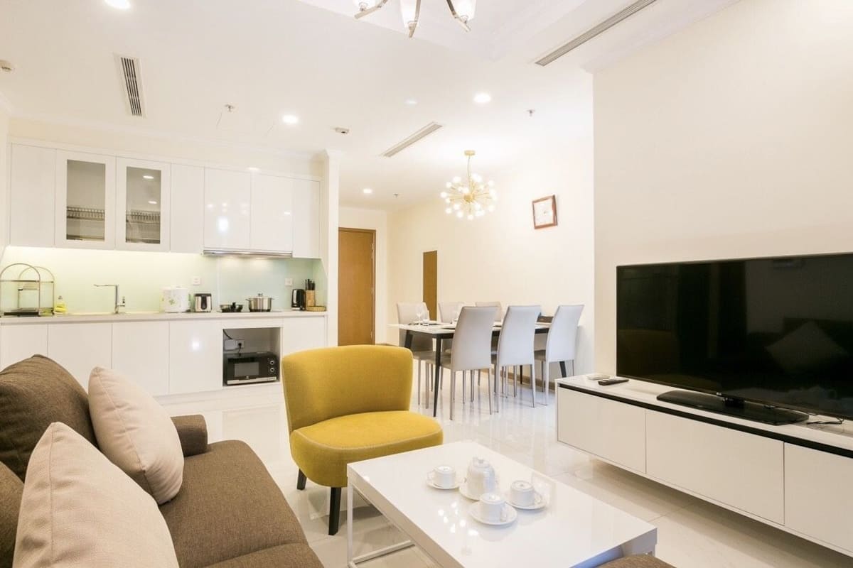 Ein modernes Wohnzimmer mit einer Couch, einem gelben Sessel, einem Couchtisch, einem Fernseher und einem Essbereich mit Stühlen und einem Tisch.