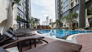 A pool area with lounge chairs and umbrellas, surrounded by tall buildings and greenery. - LANDMARK PLUS RESIDENCES LUXURY SUITE (Ho Chi Minh City)