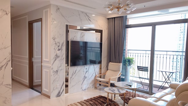 A modern living room with a flat-screen TV, a sofa, a coffee table, and a balcony with outdoor furniture. - LANDMARK PLUS RESIDENCES LUXURY SUITE (Ho Chi Minh City)