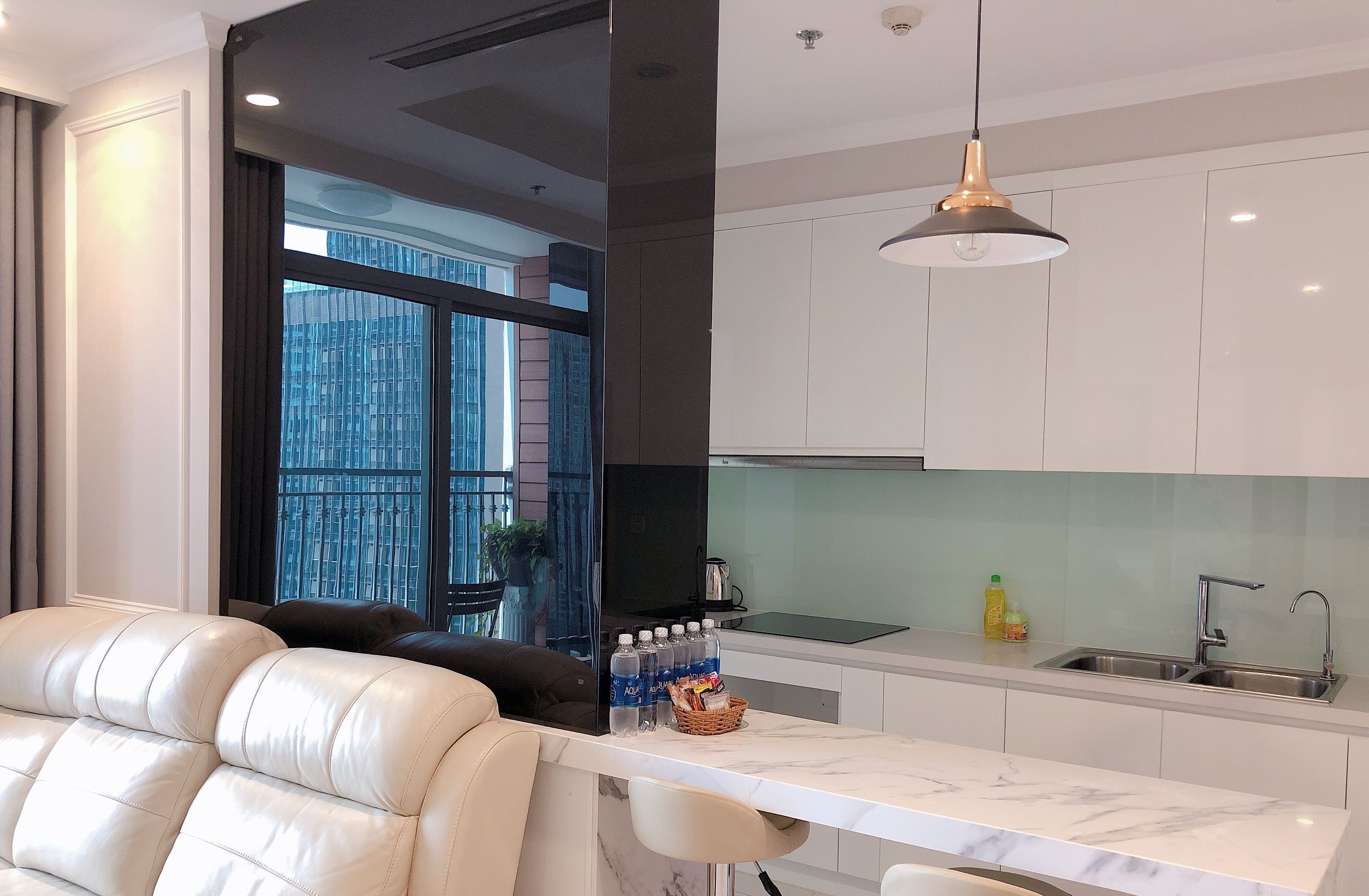 A modern kitchen with white cabinets, a marble countertop, and a large window offering a view of buildings.