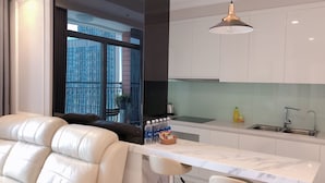 A modern kitchen with white cabinets, a marble countertop, and a large window offering a view of buildings. - LANDMARK PLUS RESIDENCES LUXURY SUITE (Ho Chi Minh City)
