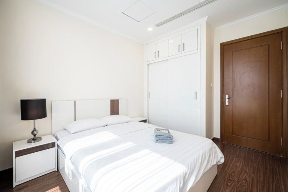A hotel room with a bed, a nightstand, a lamp, a wardrobe, and a door.