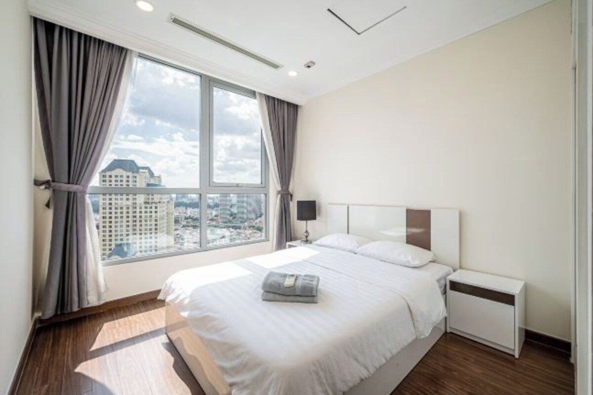 Una habitación de hotel moderna con una cama grande, una mesita de noche y una ventana con cortinas.