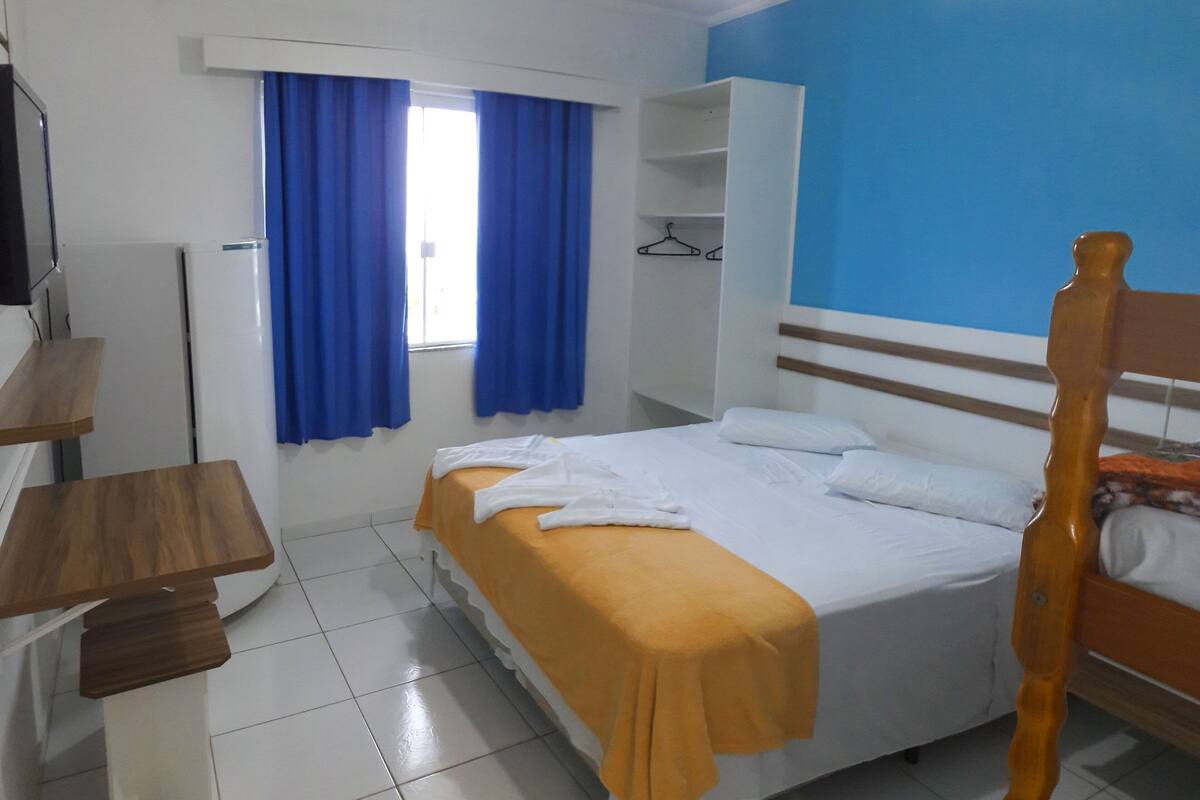 A hotel room with a bed, a desk, a wardrobe, and a window with curtains.