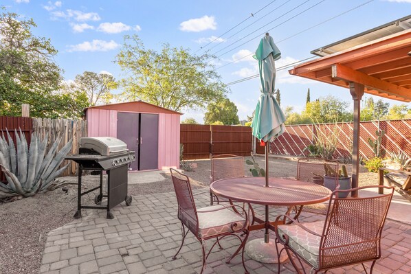 An outdoor patio with a grill, metal chairs, and a covered area.