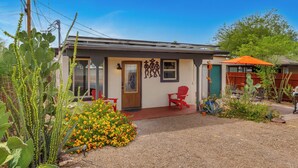 A small building with a door, windows, and a red chair outside. - The Tucsonan Style Casita - FULLY FENCED AND PET FRIENDLY! (Tucson)