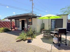 A patio with a grill, a table, and chairs, surrounded by potted plants and a cactus.