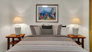A bedroom with a bed, two bedside tables, a lamp on each, a framed painting on the wall, and a door. - The Tucsonan Style Casita - FULLY FENCED AND PET FRIENDLY! (Tucson)
