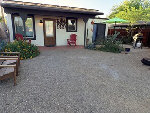A house with a gravel driveway, a wooden bench, a red chair, a cactus, and a green umbrella.