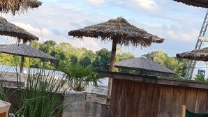 Una terrassa de fusta amb sombrerets de palla, una banca de fusta i una cadira.