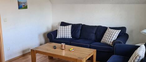 Un salón con una mesa de centro de madera, un sofá azul y un cuadro colgado en la pared.