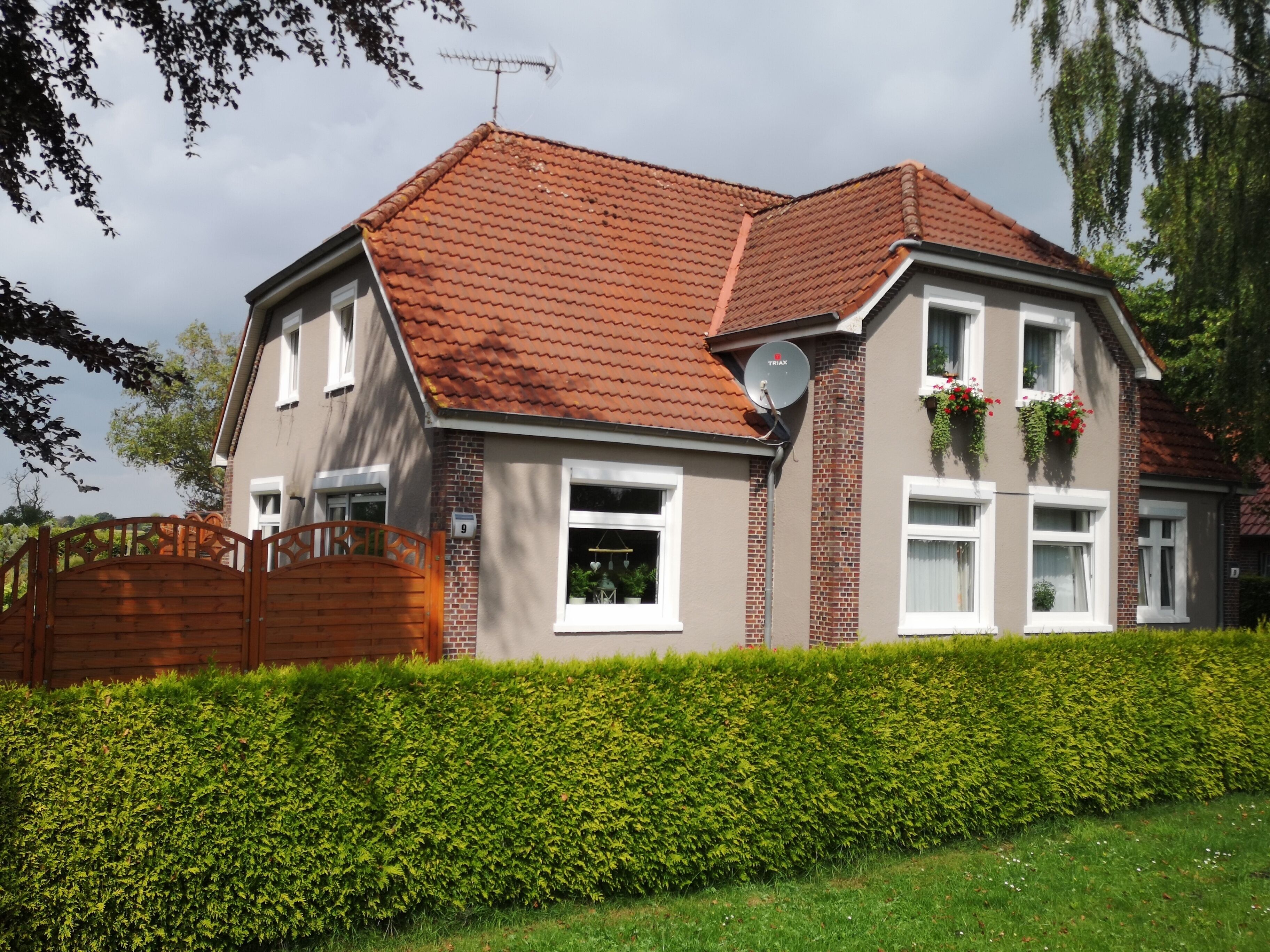 A two-story house with a red-tiled roof, a satellite dish, and a number '9' on the wall.