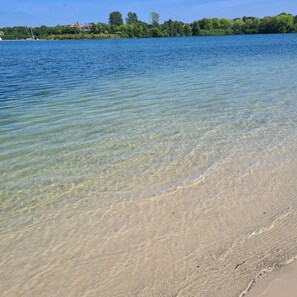 A clear view of a beach with calm water, a sandy shore, and a distant shoreline with buildings and trees. - Feel-good apartment in East Frisia: perfect for couples & business trips, Aurich Ogenbargen (Ogenbargen)