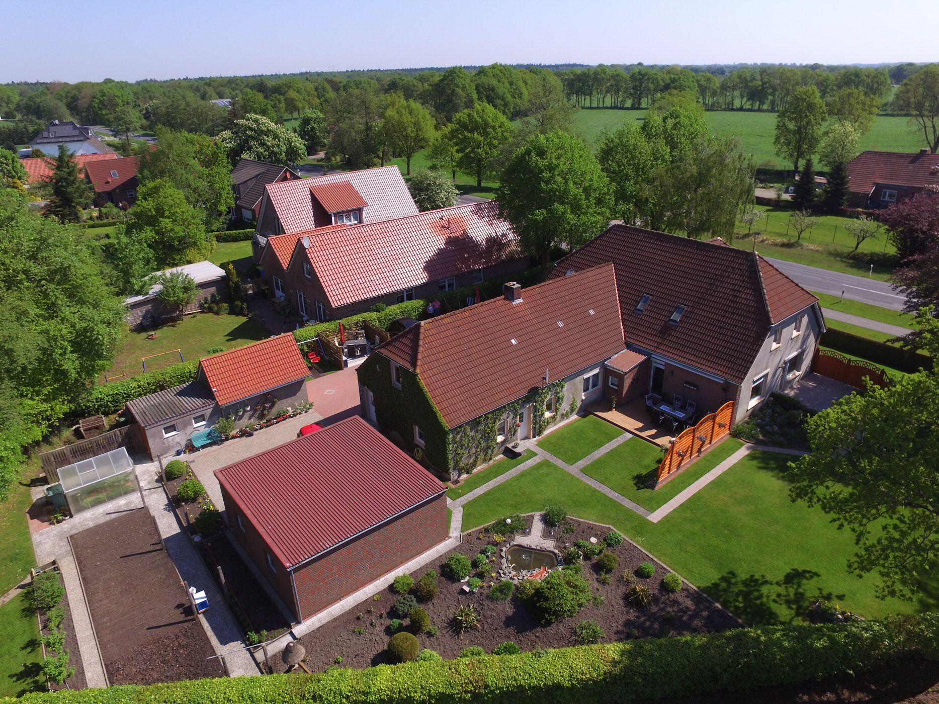A residential area with multiple houses, each featuring red-tiled roofs and surrounded by green lawns and trees.