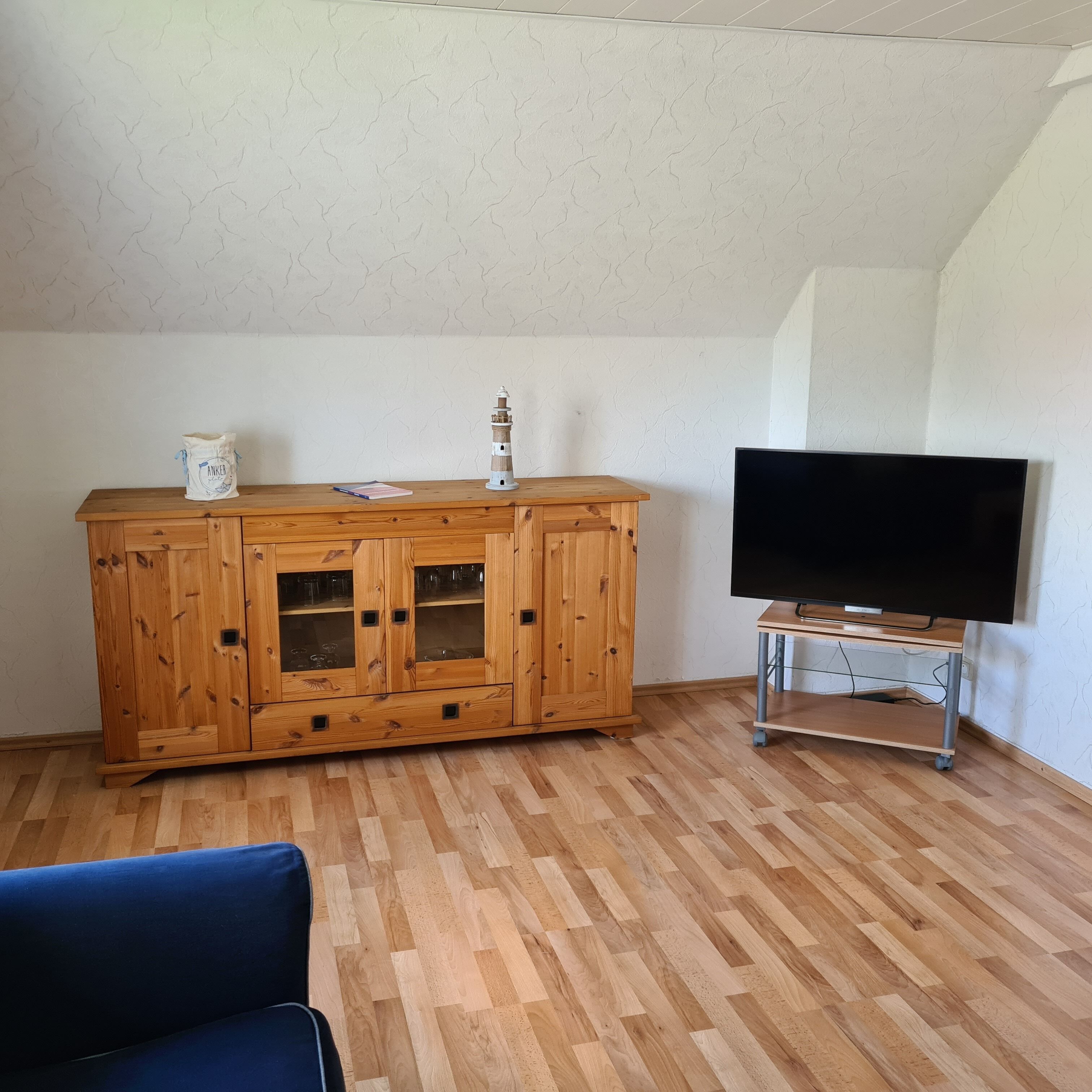 Ein Zimmer mit einem Holzschrank, einem Fernseher auf einem Schrank und einem blauen Sessel.