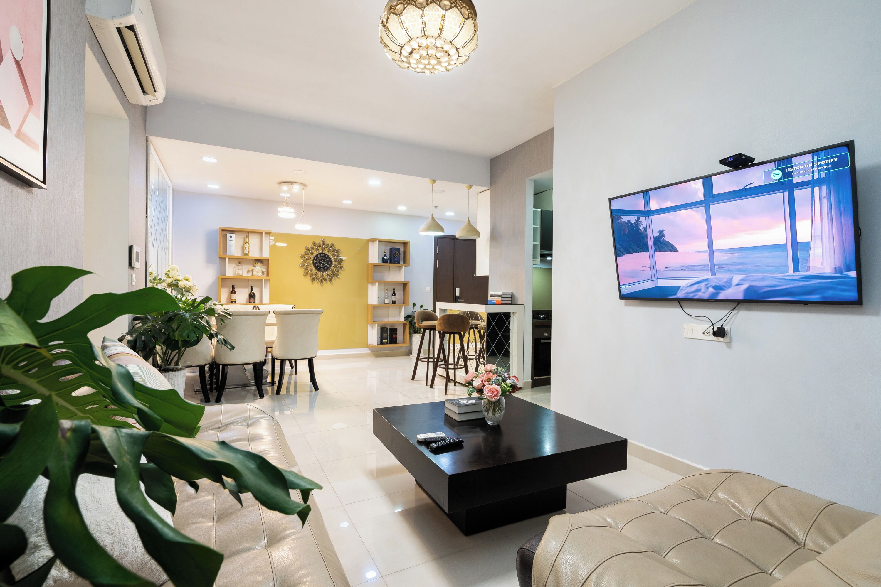 A modern living room with a black coffee table, a beige sofa, and a large flat-screen TV displaying a beach scene.