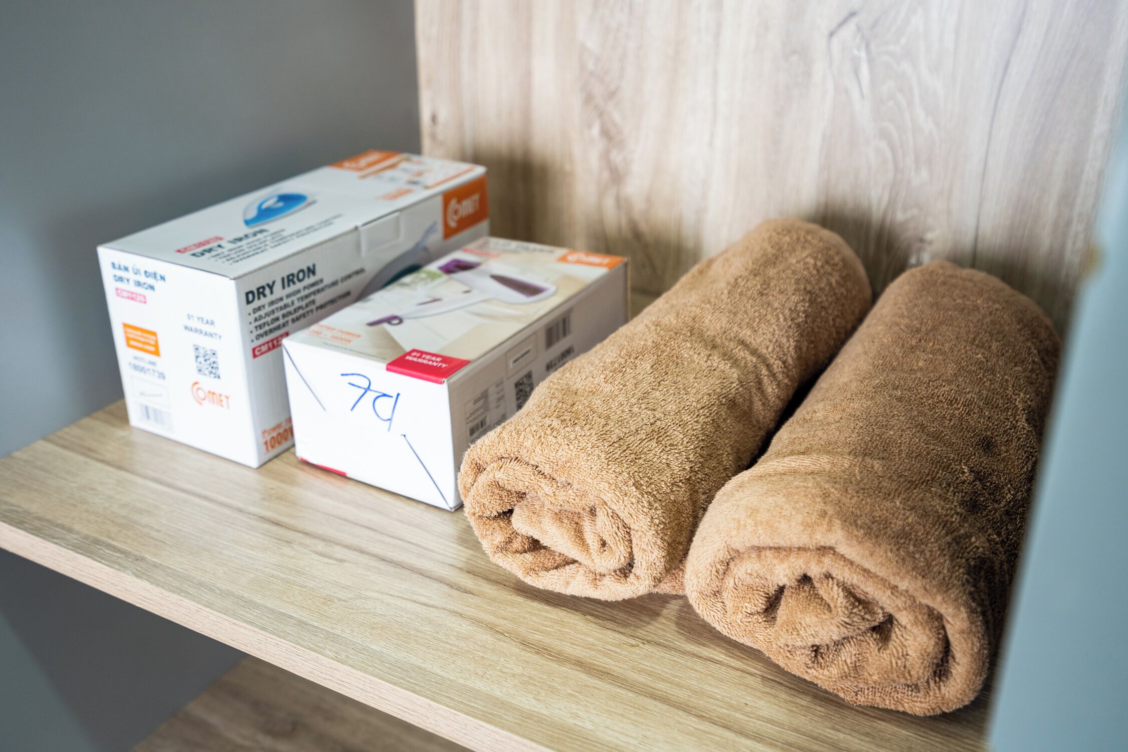 Une étagère en bois sur laquelle sont posés deux serviettes enroulées et deux boîtes de produits à repasser.