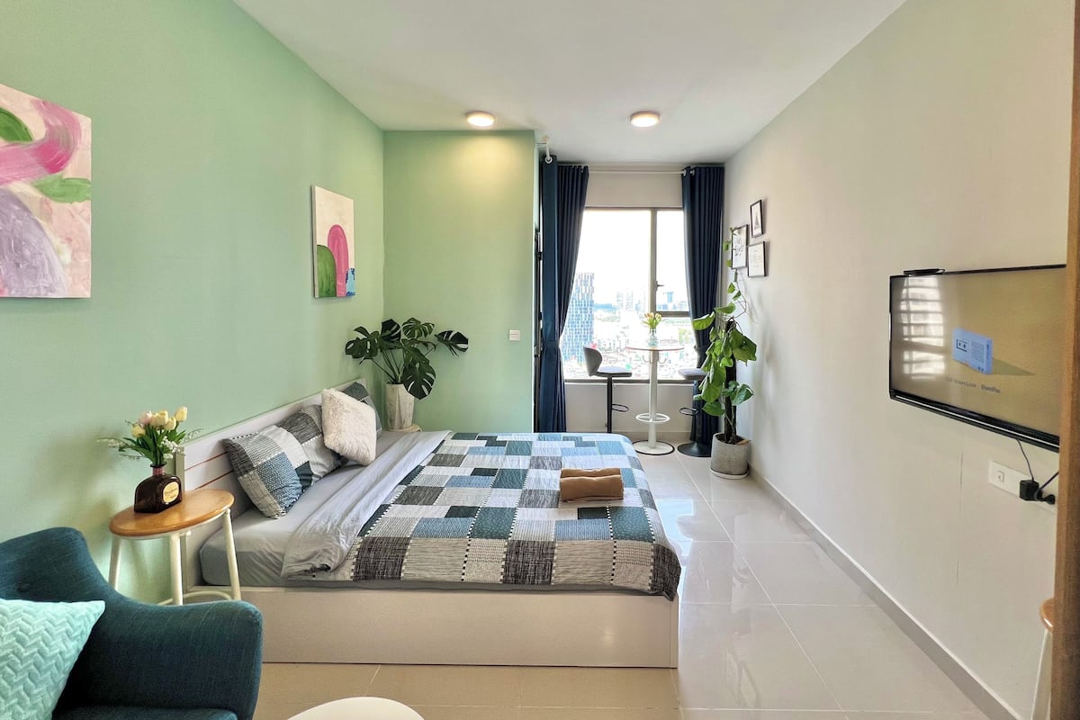 A bedroom with a bed, a chair, a small table, and a potted plant.