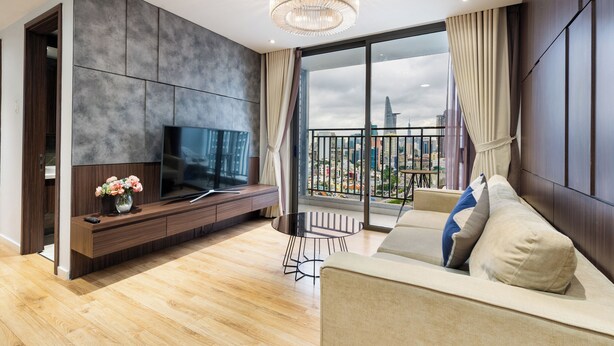 A modern living room with a flat-screen TV, a sofa, a small round table, and a balcony with a city view.
