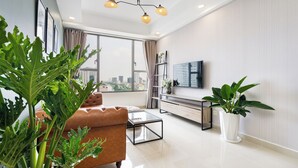 A modern living room with a brown sofa, a glass coffee table, a TV on a stand, and large windows with a city view.