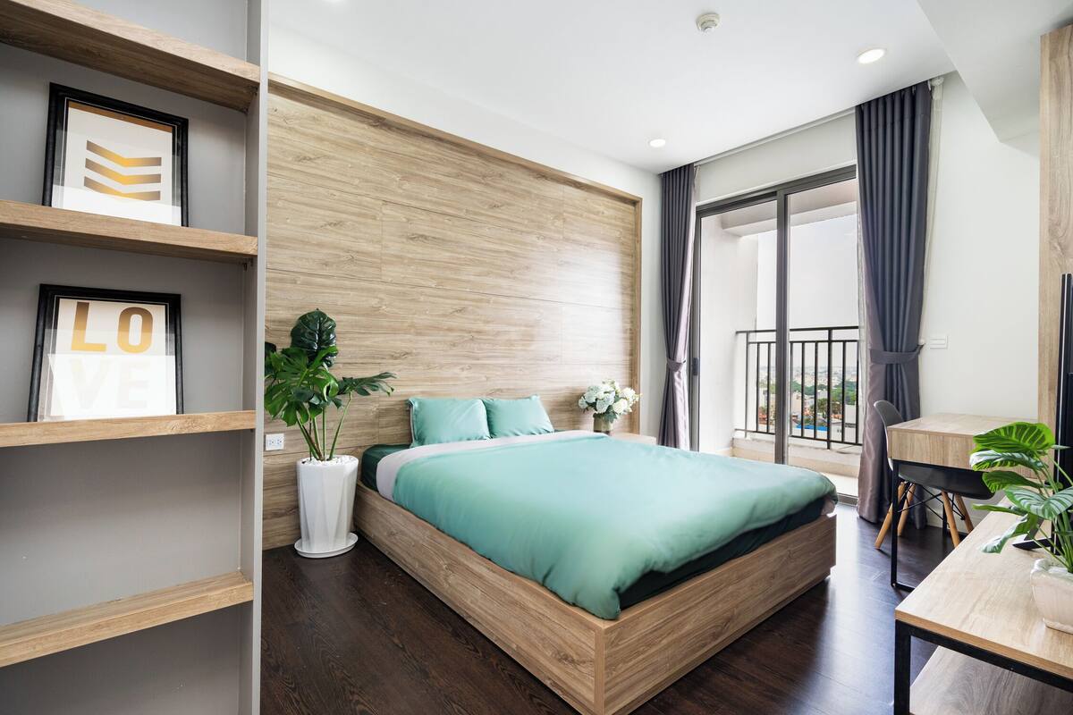 A modern bedroom with a wooden bed frame, a green bedspread, and a large window with a balcony.