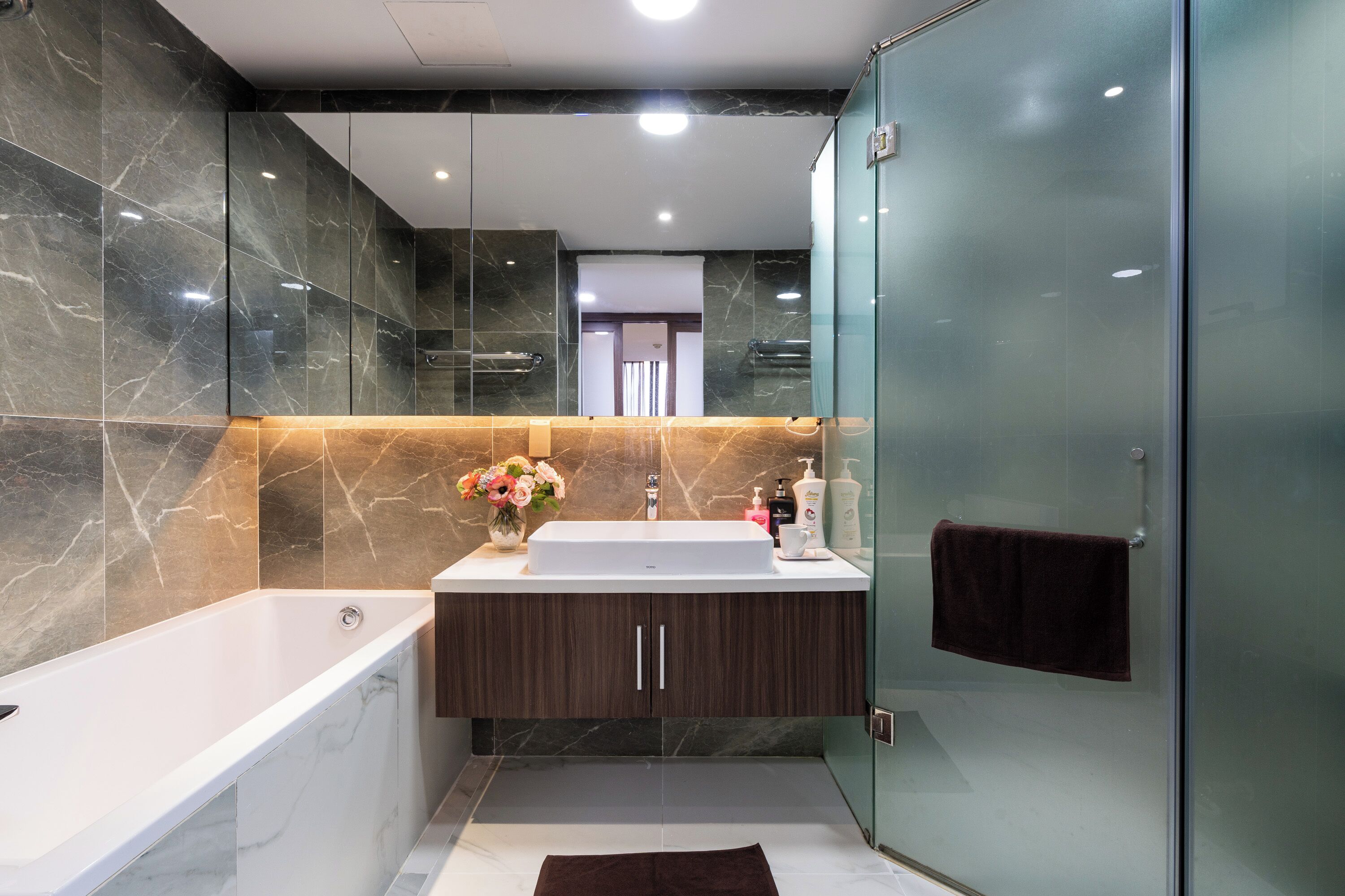 A modern bathroom with a marble vanity, a bathtub, and a glass shower enclosure.
