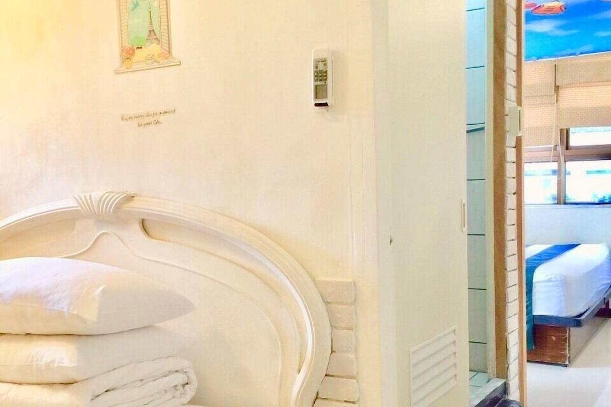 A hotel room with a white headboard, a small painting of the Eiffel Tower, and a view of a beach through a window.