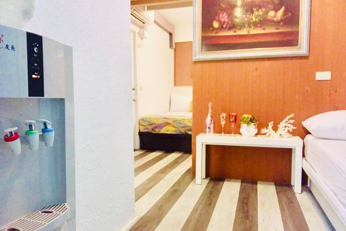 A hotel room with a striped floor, a bed with a colorful bedspread, a white bedside table with decorative items, and a wall-mounted painting.