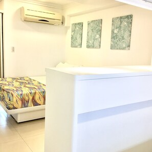 A room with a bed, an air conditioning unit, and three framed artworks on the wall.