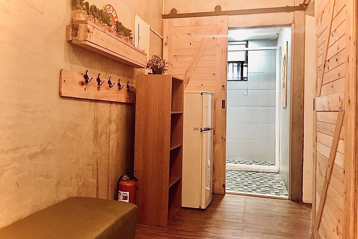 A narrow hallway with wooden walls, a bench, a shelf with decorative items, and a door leading to a bathroom with a tiled floor.