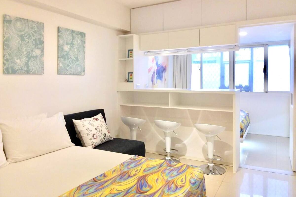 A modern bedroom with a bed, a sofa, a colorful blanket, a TV, and a minibar.