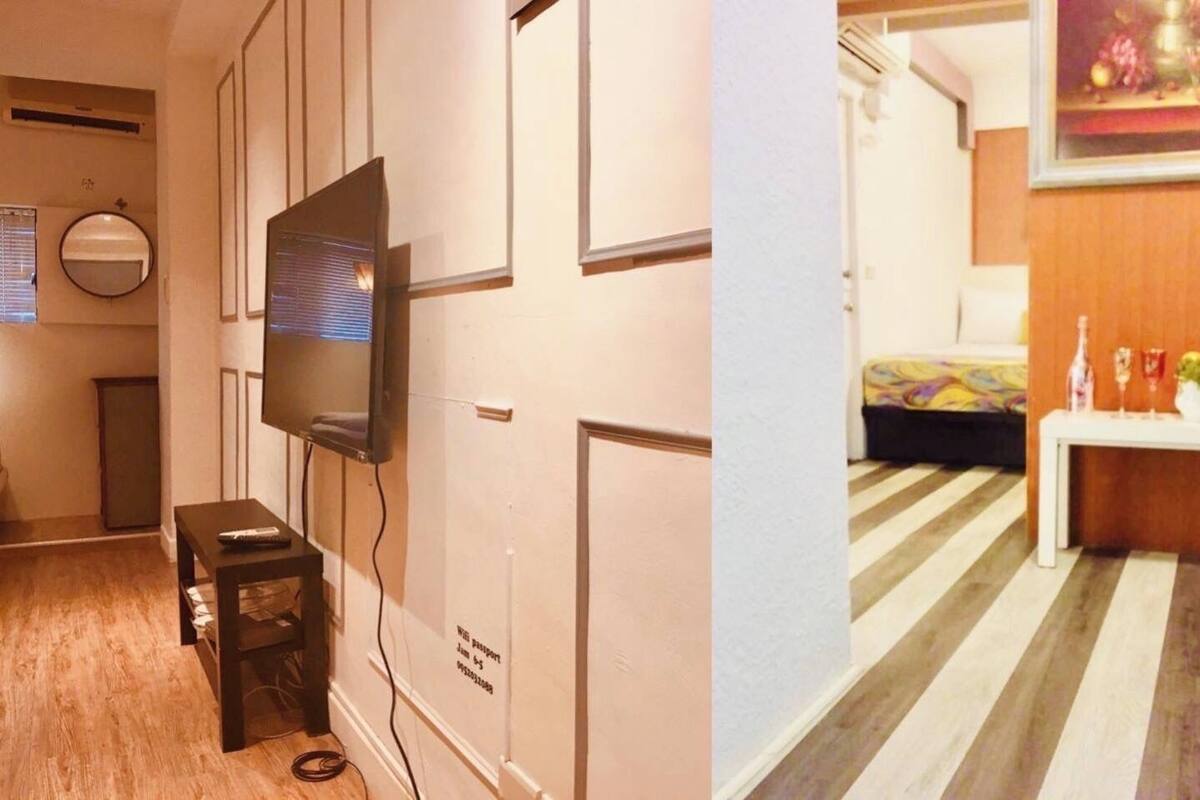 A room with a flat-screen TV mounted on the wall, a small table with a remote control, and a striped floor.