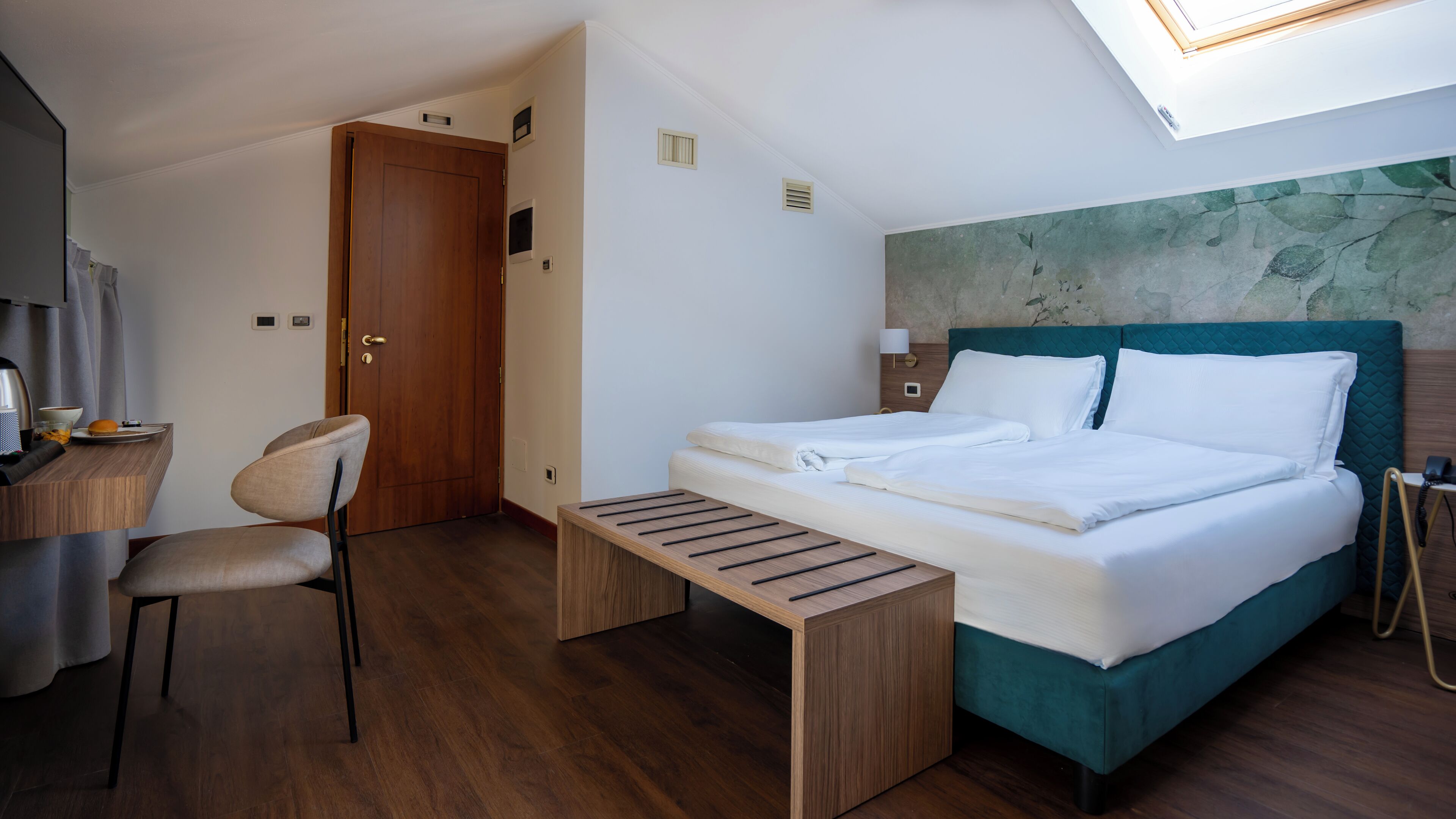 A hotel room with a bed, a desk, a chair, and a small table.